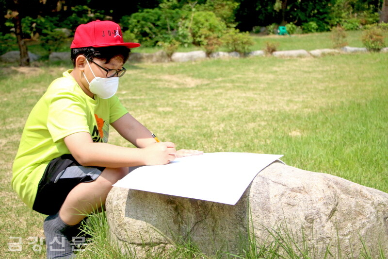 유하준(초 5) 어린이가 자연을 책상 삼아 그림을 그리고 있다.
