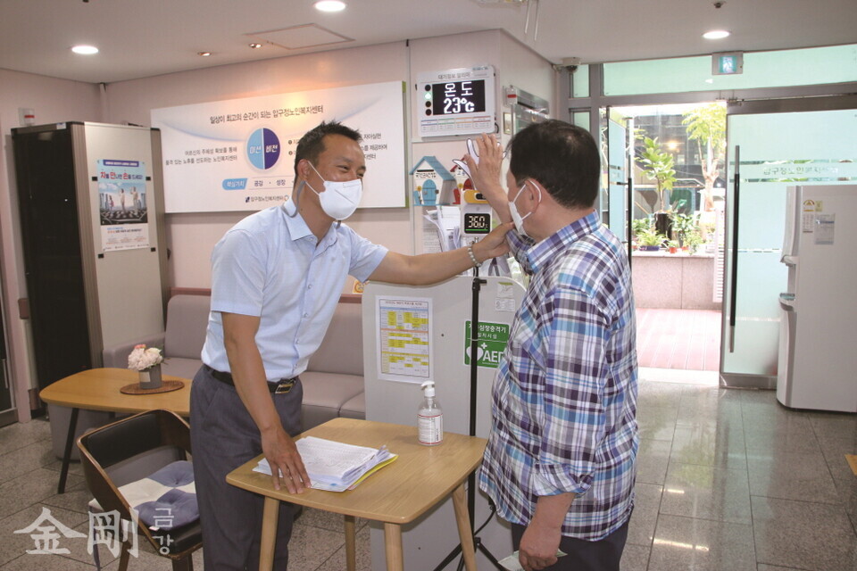 김성진 관장이 복지센터를 방문한 어르신의 체온 측정을 도와주고 있다.